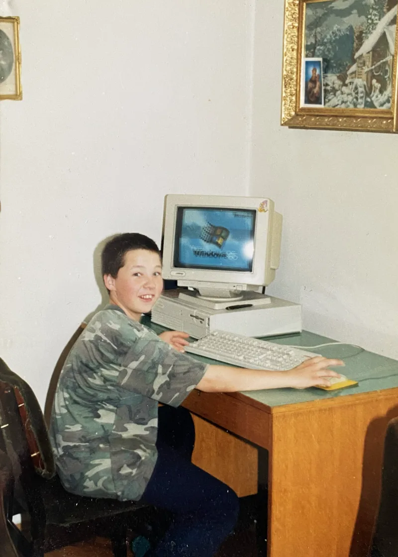 Tom as a child at his first PC, with Windows 95 on the monitor and his hand on the mouse.