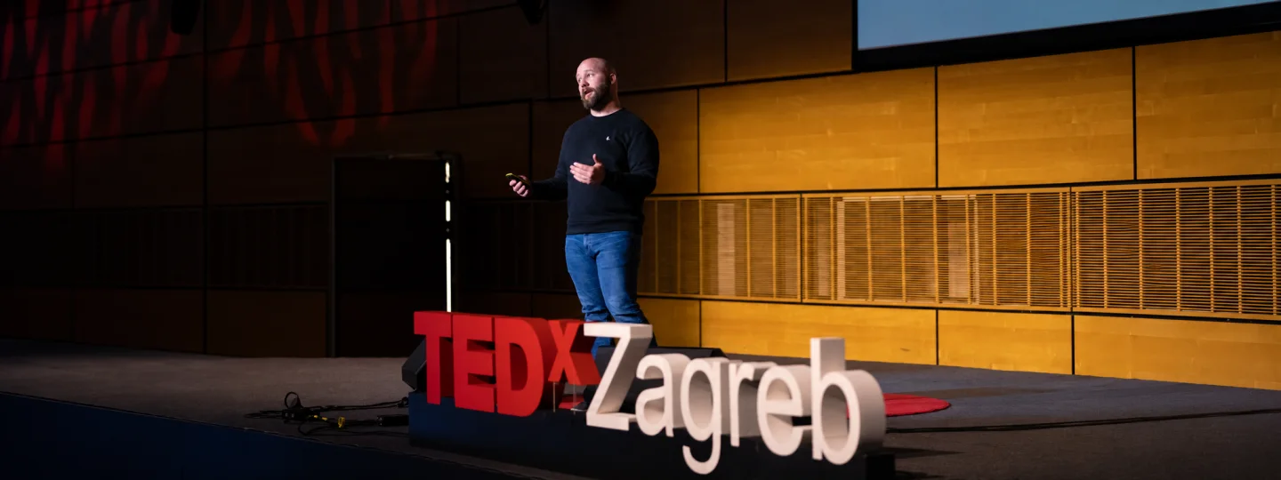 Tom giving a talk on stage behind the red and white TEDx Zagreb lettering.